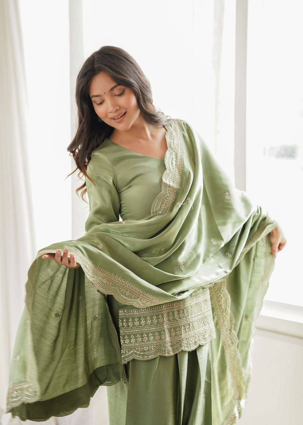 Woman wearing a green traditional outfit with a matching dupatta in bright room.